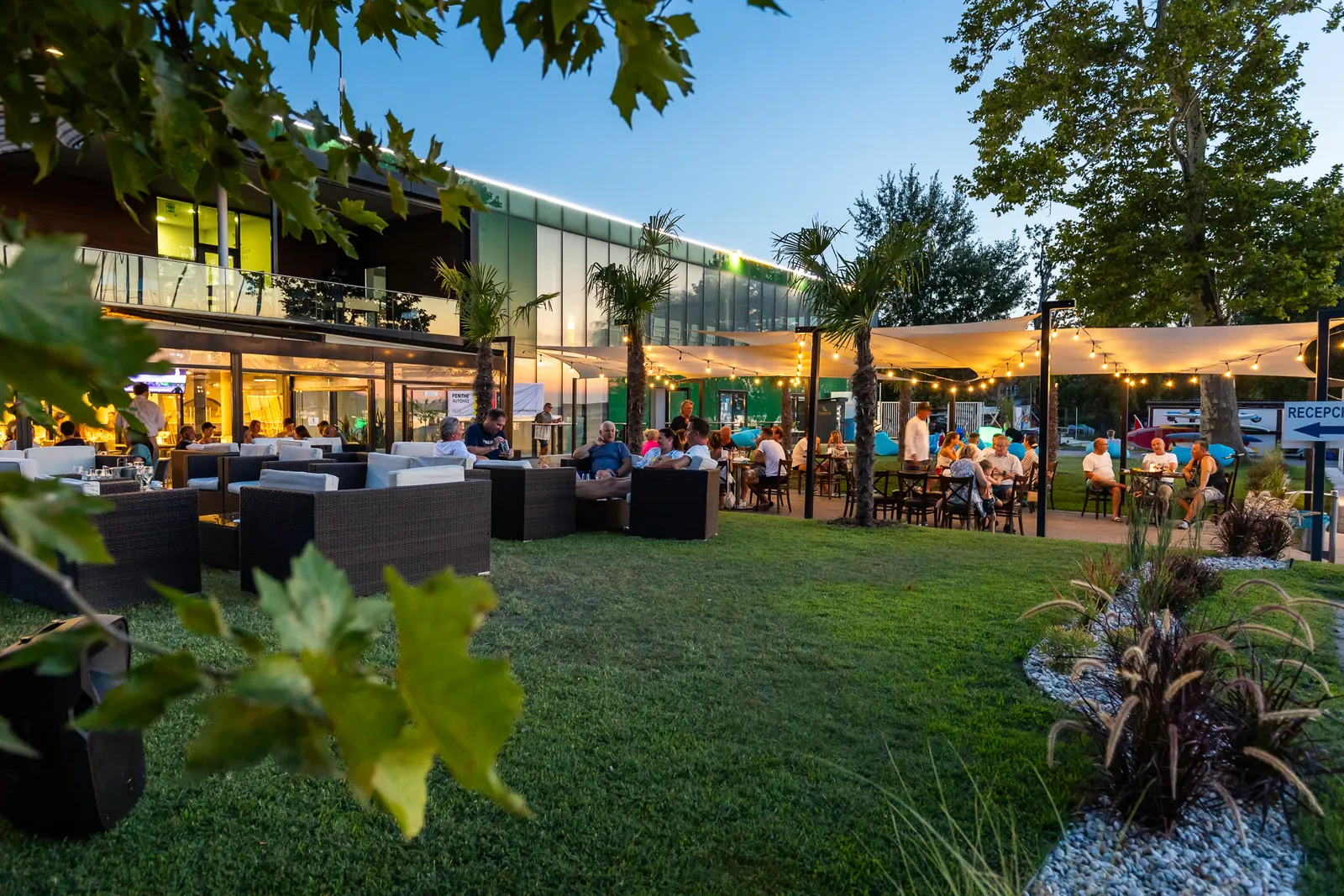 A BL Yacht Club kerthelyisége a pázsiton, napernyőkkel és a klubépülettel