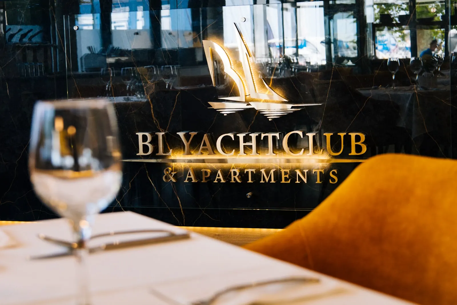 A BL Yacht Club aranyszínű felirata, előtte borospohár