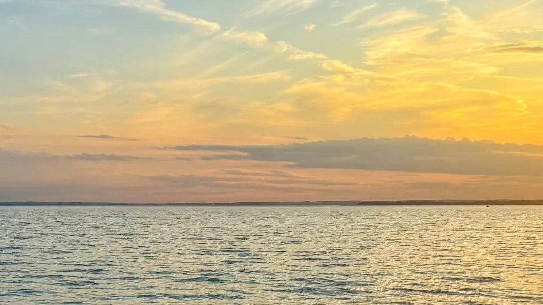 Alkonyi arany fény a Balaton vizén, a háttérben a túlpart sziluettje